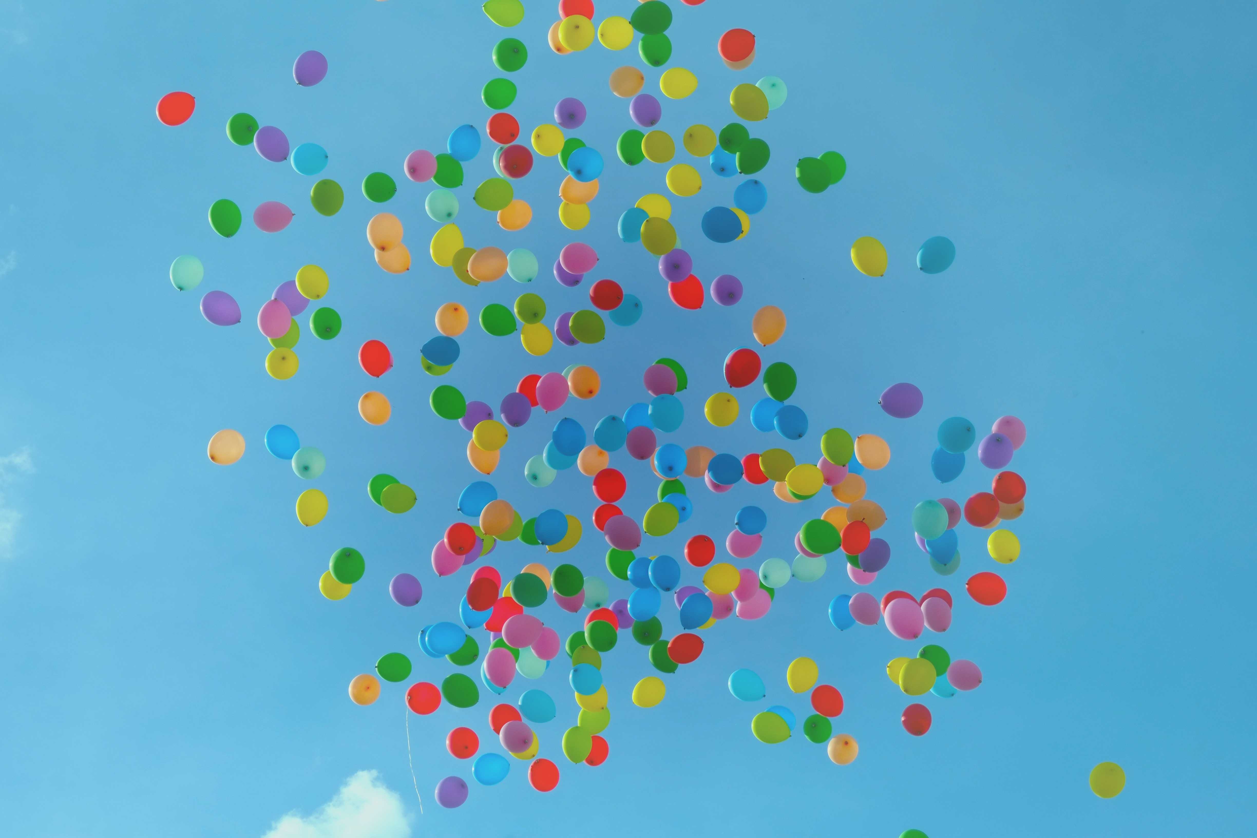 Colourful helium balloons rising into a blue sky